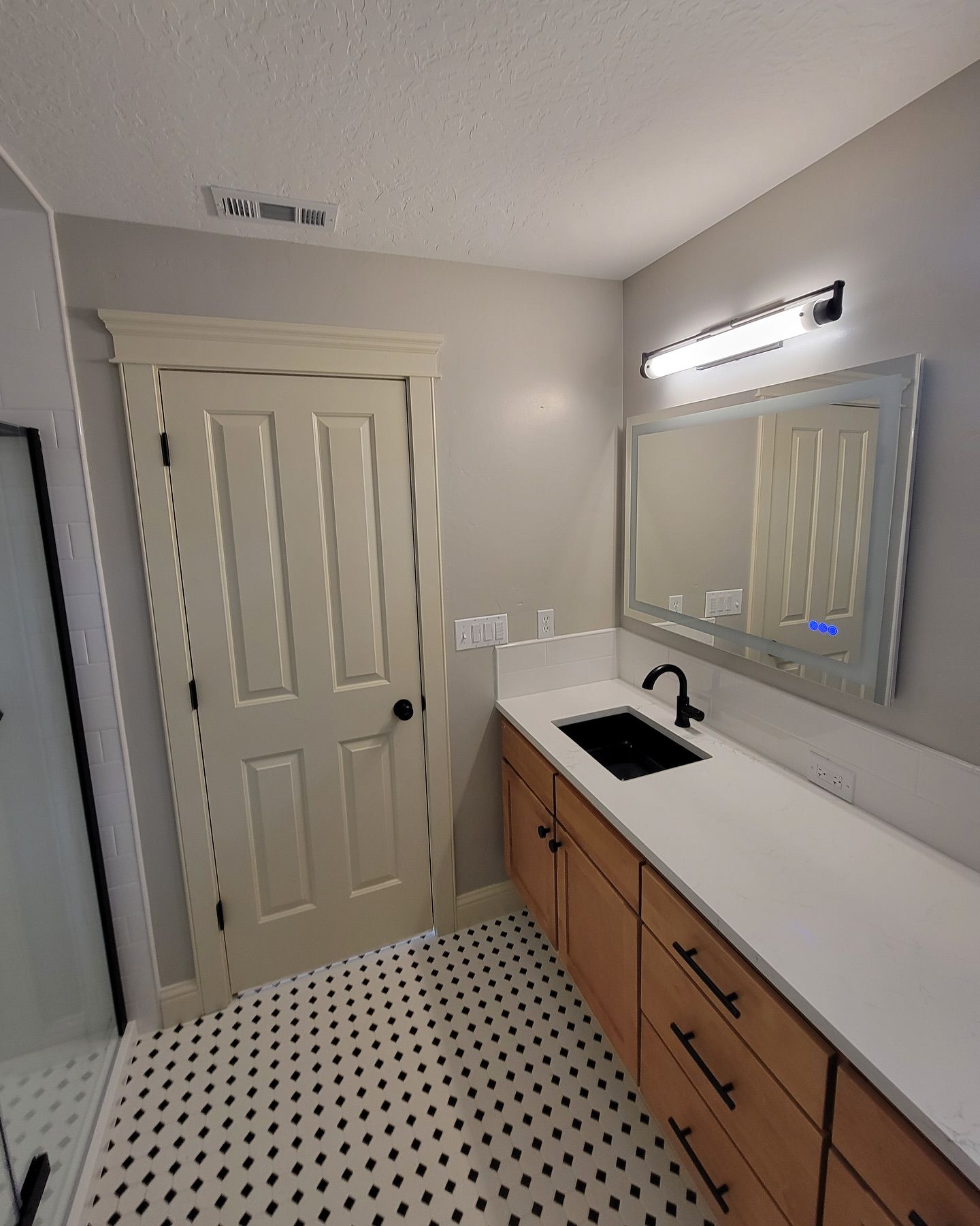 Bathroom with white countertop, wood cabinets, black sink, mirror, and black and white tiled floor.