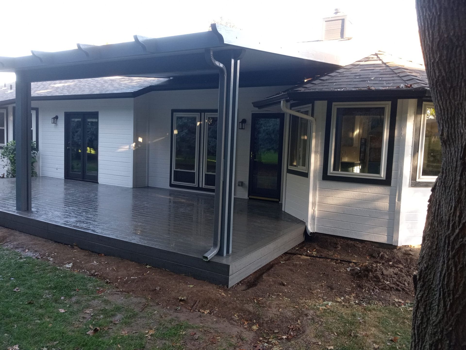 Backyard patio with a dark pergola, attached to a white house with black trim and doors.