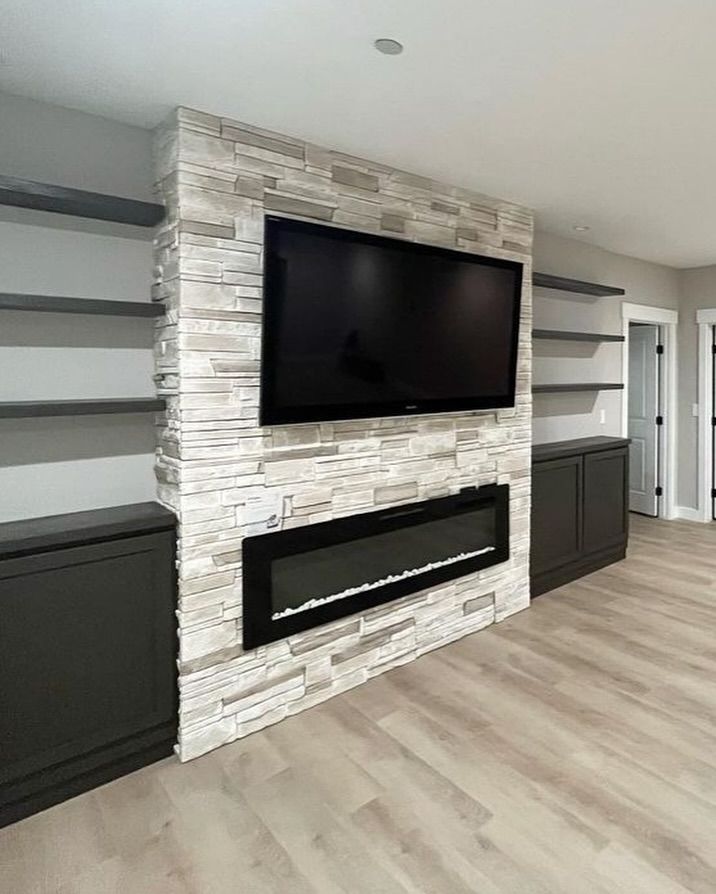 Modern living room with stone fireplace, mounted TV, and built-in shelves and cabinets.