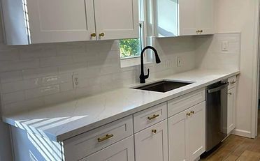 White kitchen with white countertops, cabinets, and subway tile backsplash; black faucet, and stainless steel dishwasher.