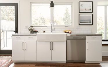 White kitchen with cabinets, a farmhouse sink, and a stainless steel dishwasher under a window.