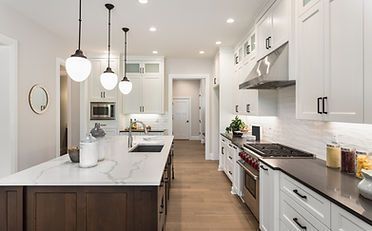Spacious white kitchen with island, pendant lights, stainless steel appliances, and wood floors.