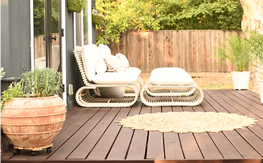 Outdoor patio with white woven seating, a round rug, and large potted plants.