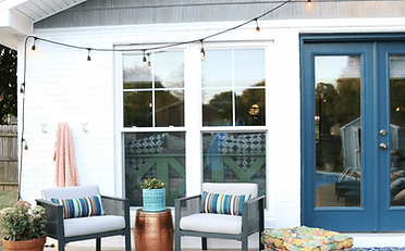 Patio with gray chairs, blue cushions, copper table, string lights, and blue door.