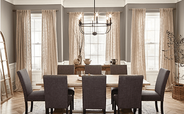 Formal dining room: table, chairs, chandelier, windows with beige curtains, and a decorative mirror.