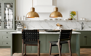 Kitchen with green cabinetry, marble backsplash, gold pendant lights, and two bar stools.