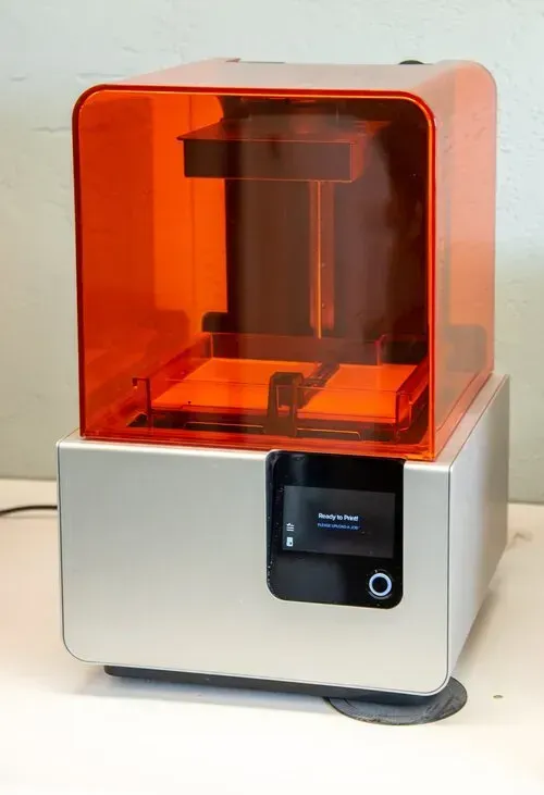 3D printer with orange translucent cover and white base, shown on a tabletop