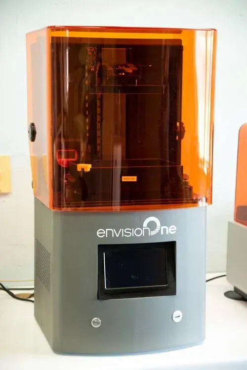 Orange-tinted 3D printer with a display screen on a gray base