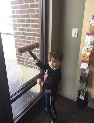 Young child with brown hair cleaning a window with a squeegee.