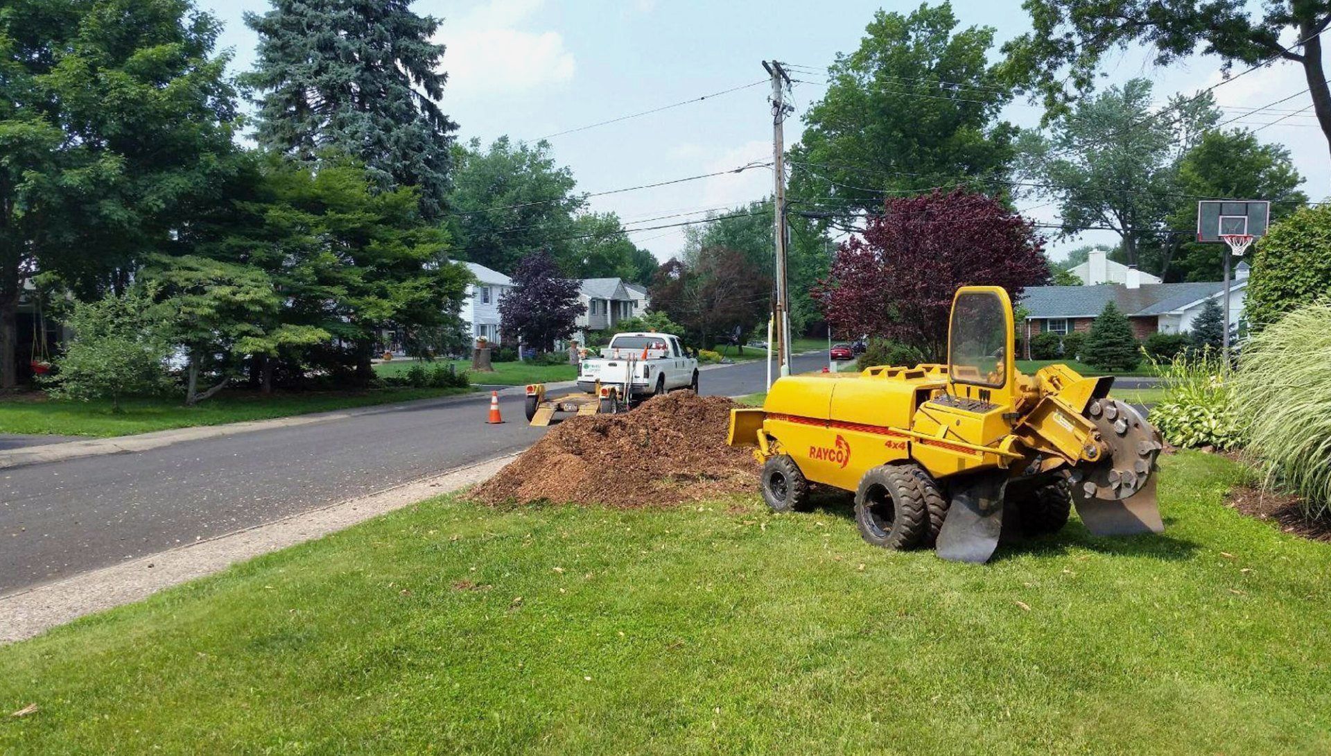 Yellow construction loader beside a roadside dirt pile in a suburban neighborhood