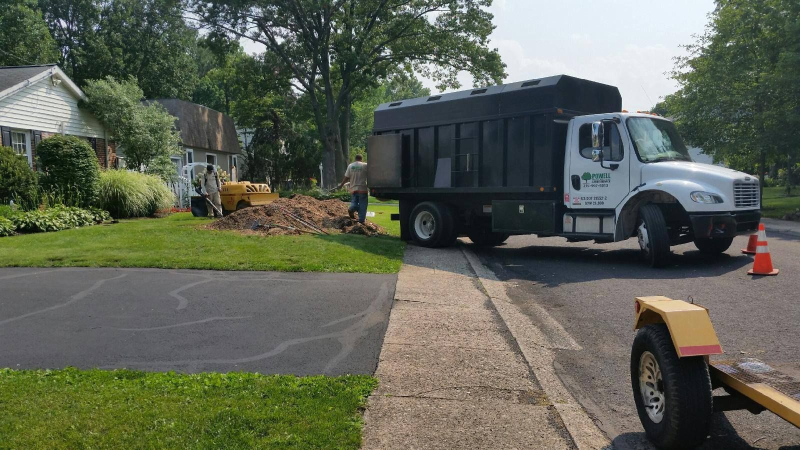 Large work truck parked by a suburban driveway, with landscaping debris and a trailer in the foreground