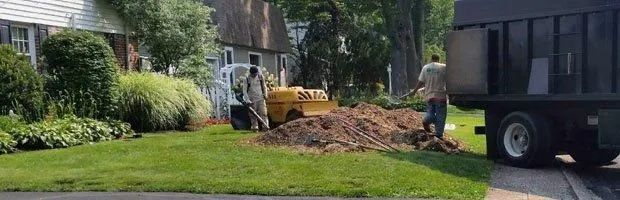 Backyard excavation with a yellow loader and dump truck beside a pile of dirt near a house