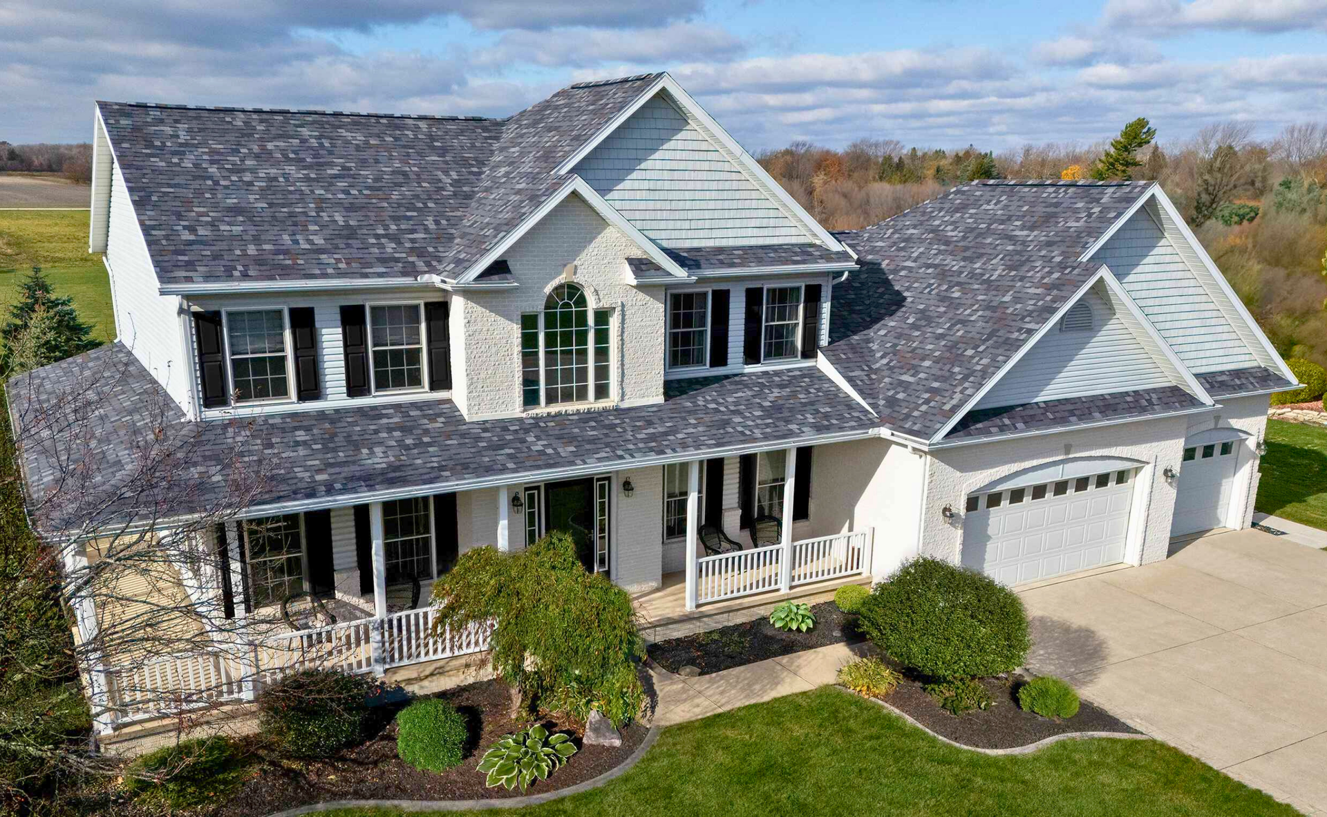 Two-story white house with gray roof and black shutters, porch, garage, and landscaped yard.