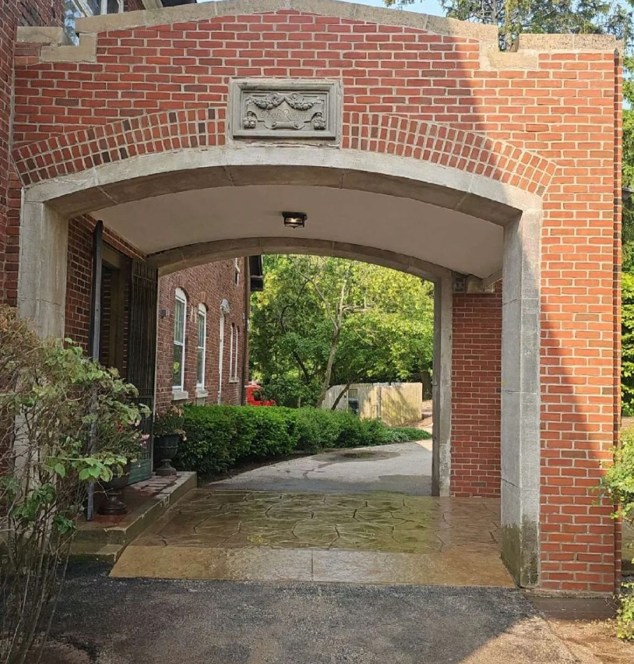 Brick archway leading to a shaded area, with concrete floor and a stone emblem above.