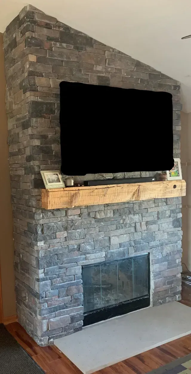 Stone fireplace with black TV, wooden mantel, and glass-door firebox.