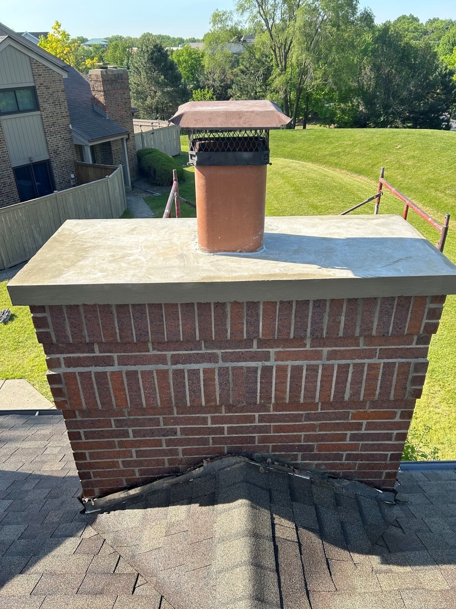 Brick chimney with copper cap on a rooftop, overlooking a grassy yard and trees