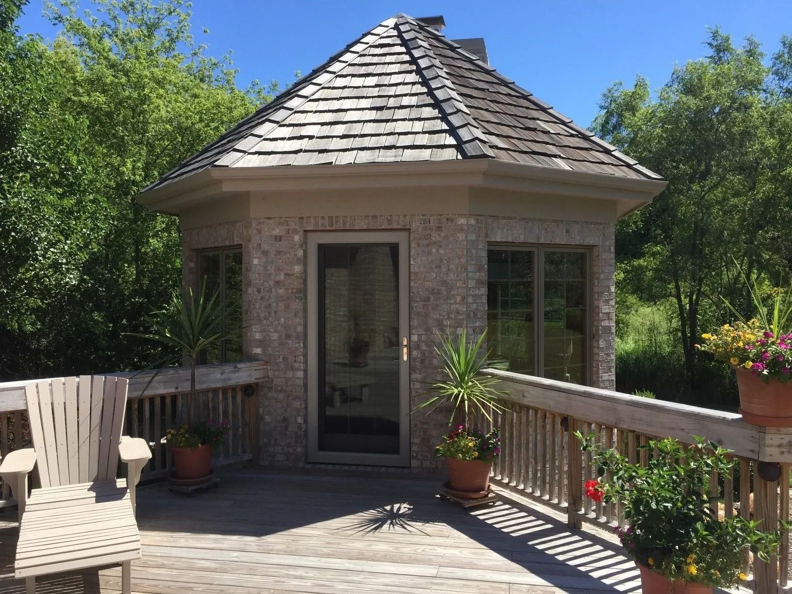 Octagonal brick building with wooden deck, potted plants, and cedar shake roof.