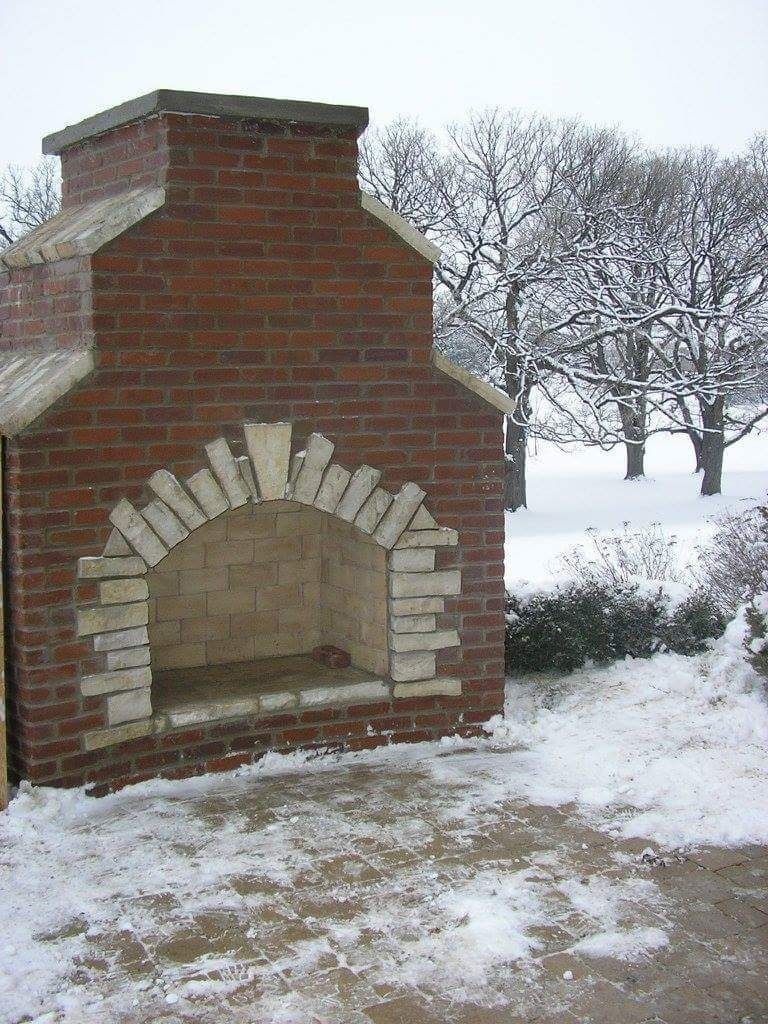 Brick outdoor fireplace, snow on the ground and in the trees in the background.