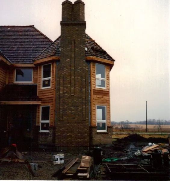 House under construction with a brick chimney, wooden siding, and several windows.