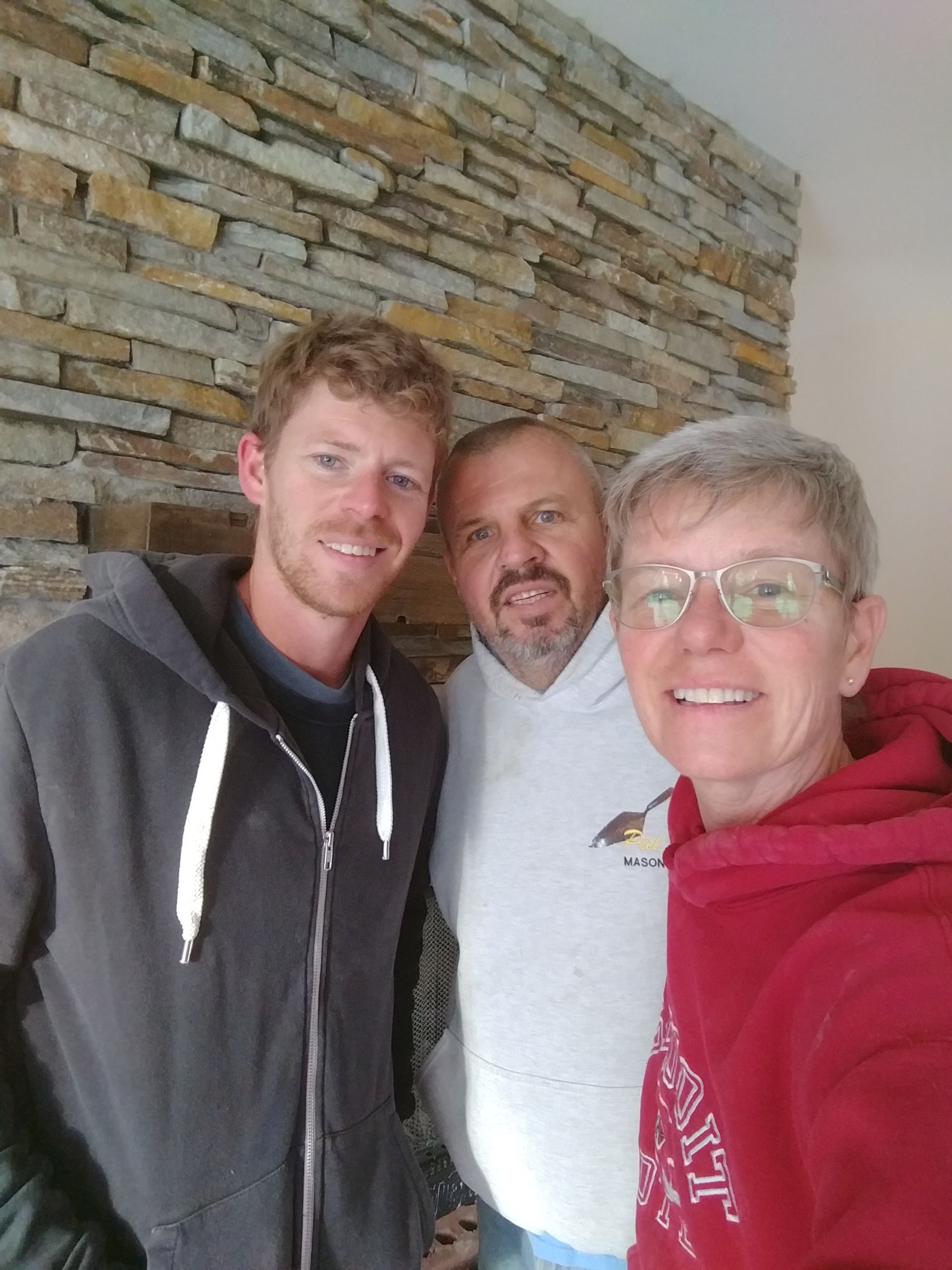 Three people smiling and posing for a photo in front of a stone wall.