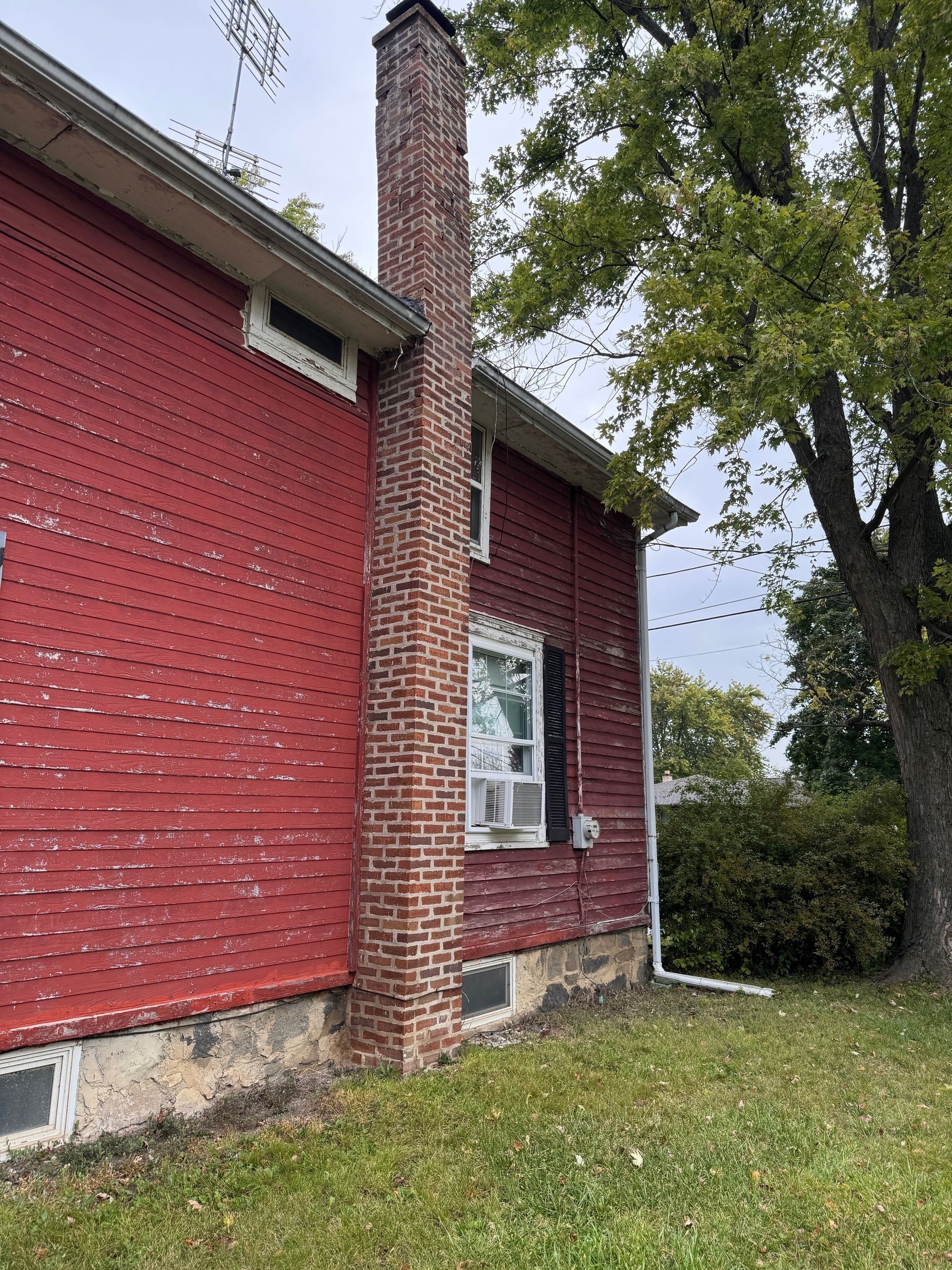 Red brick building with tall brick chimney next to a tree, on a grassy lawn.