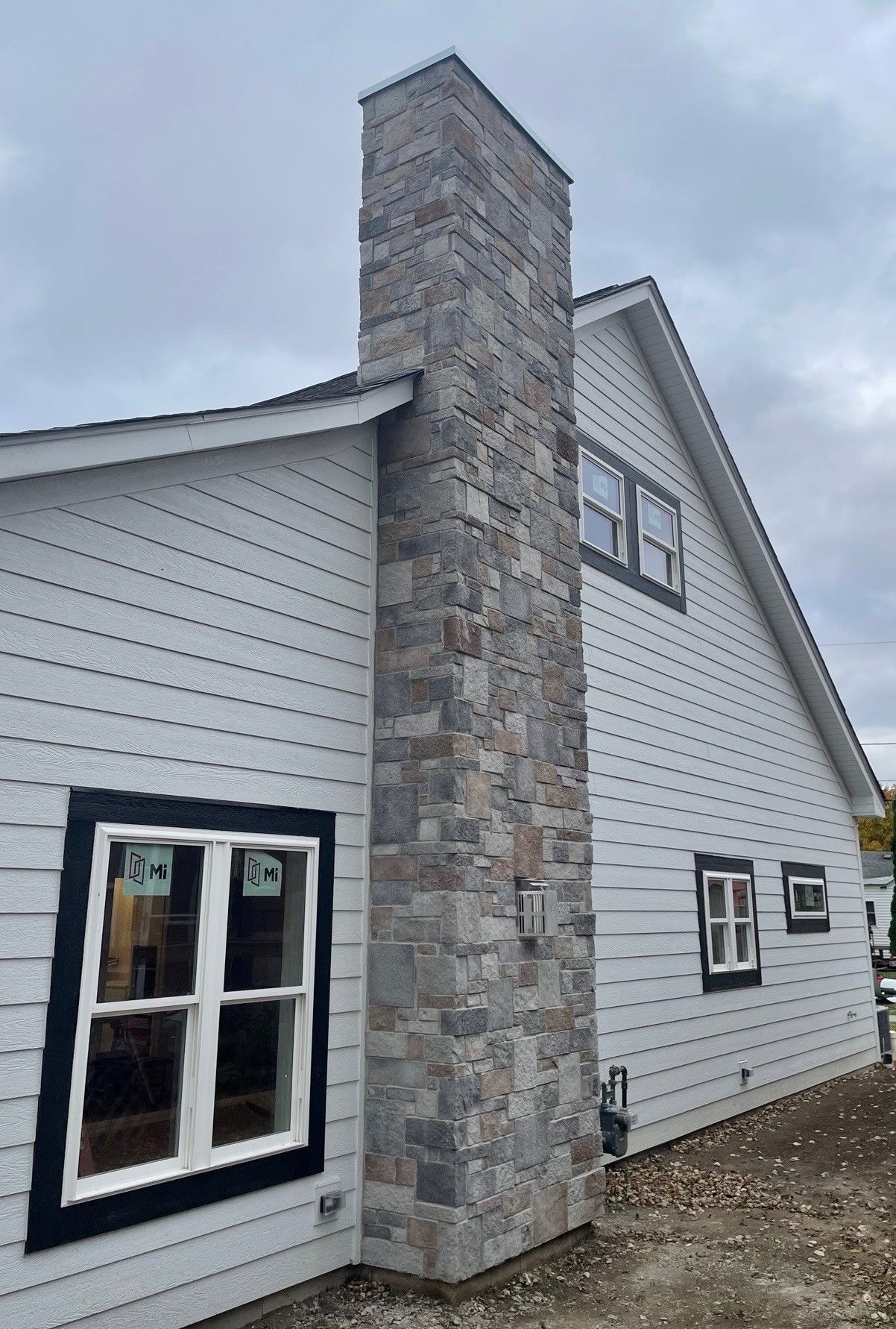 Stone chimney on a white-sided building with black-framed windows; cloudy sky.