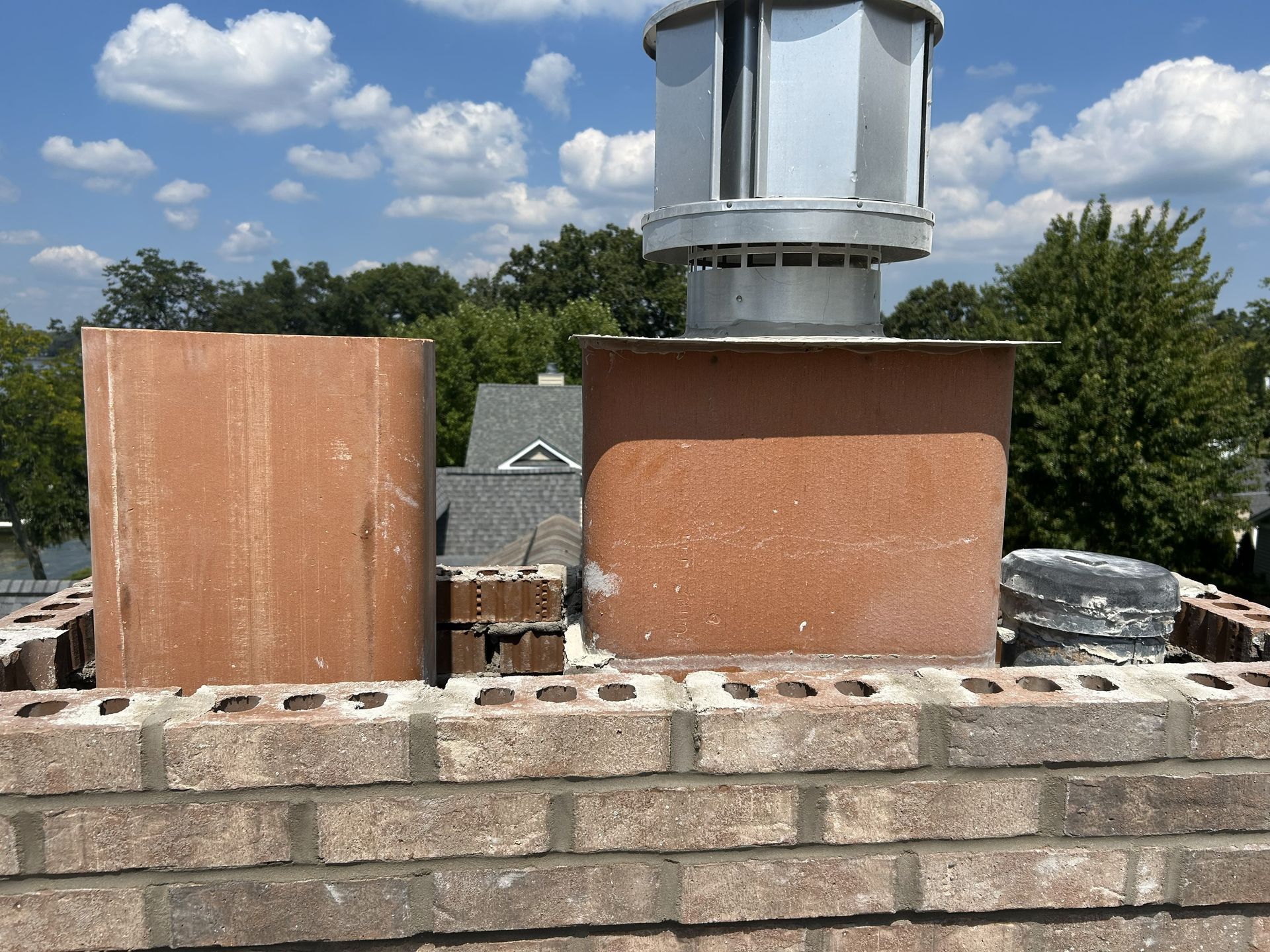 Two brick chimneys with metal caps on a rooftop against a blue sky.