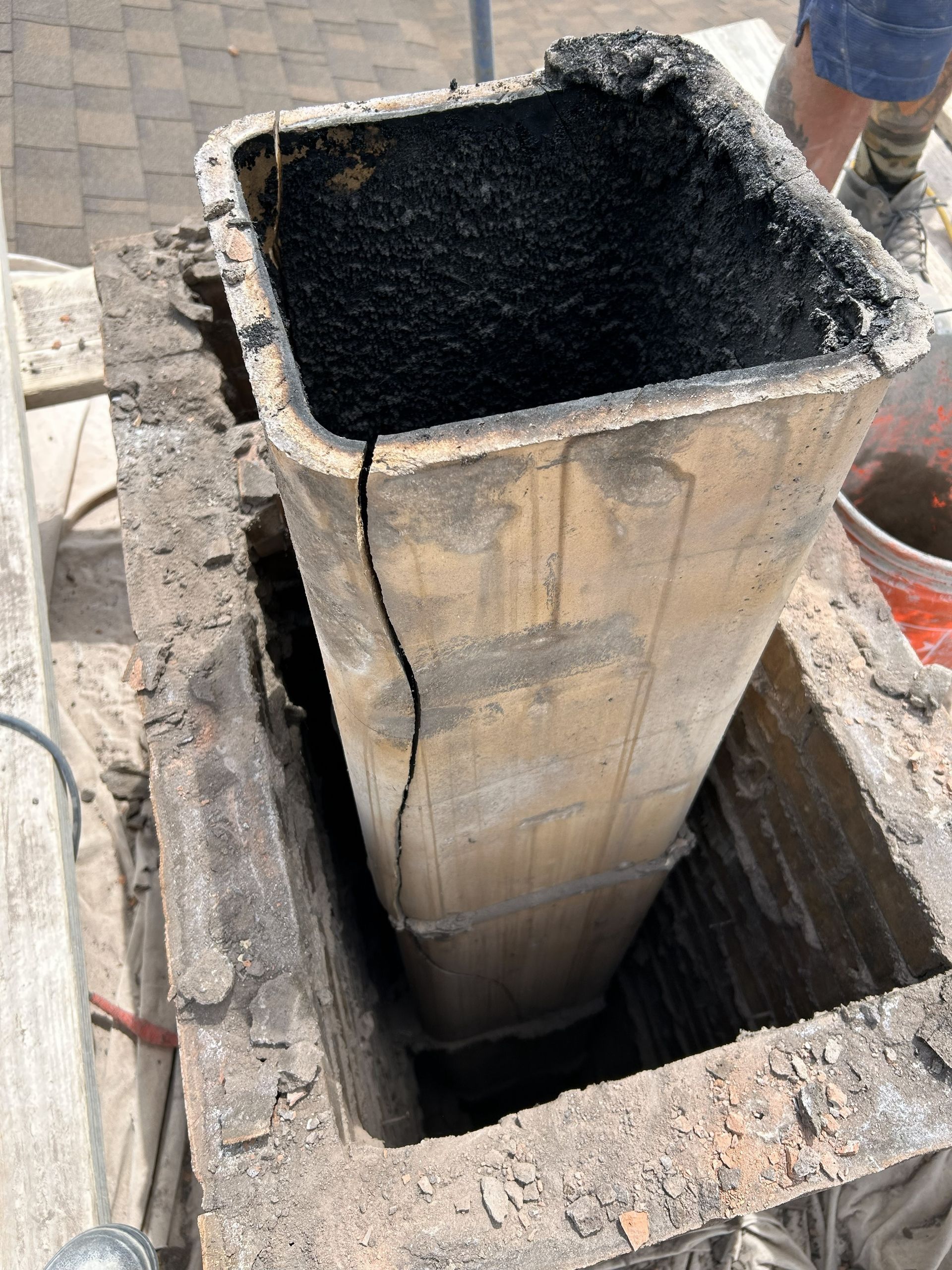 A cracked chimney flue with soot inside, set within a brick structure on a roof.