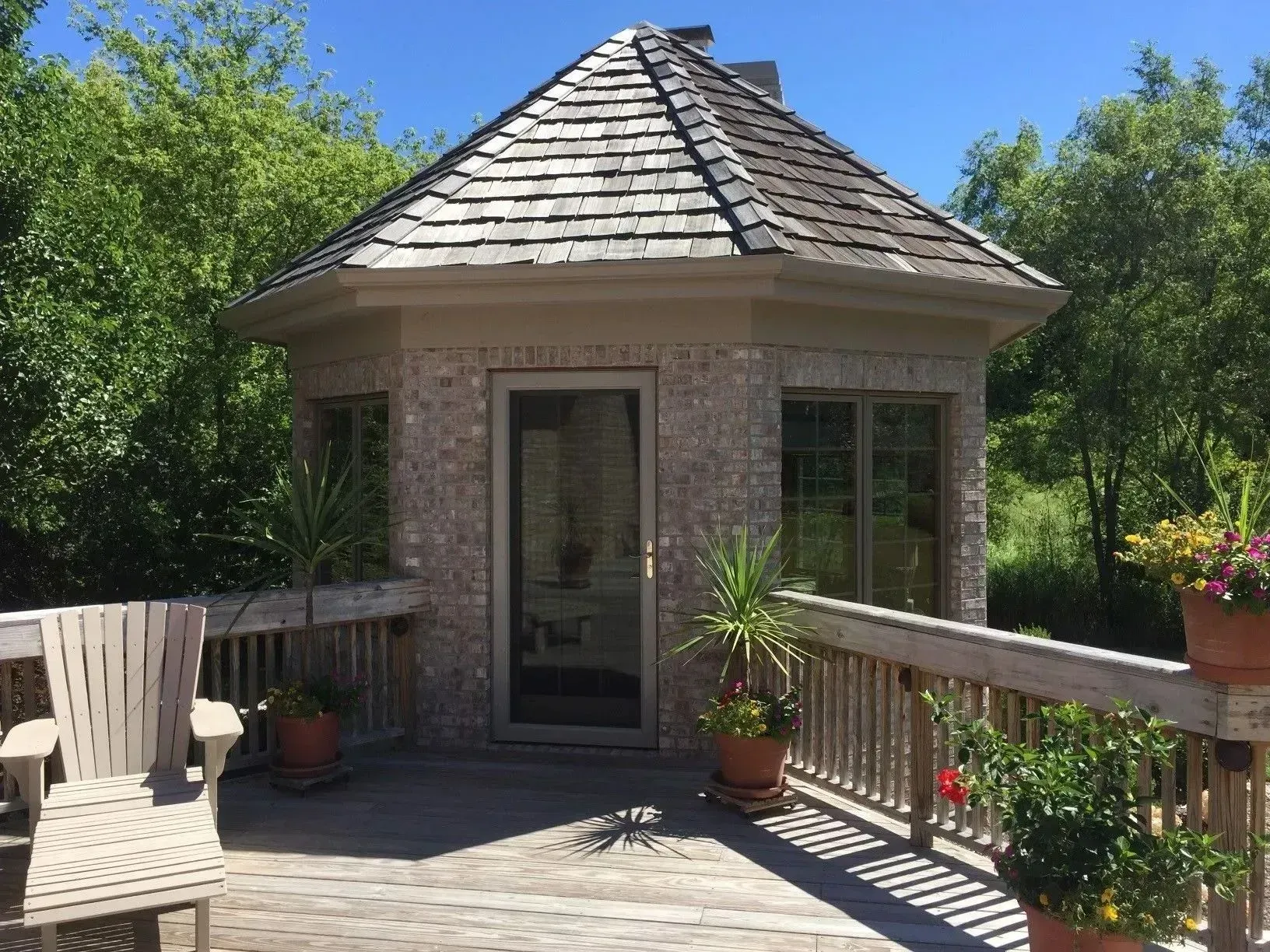 Wooden deck with a gazebo-like building. Plants in pots and wooden chair.