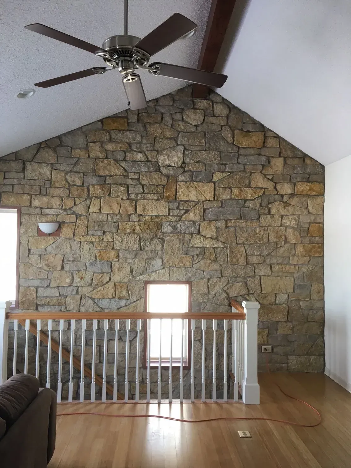 Stone wall interior with a ceiling fan, a staircase, and windows.