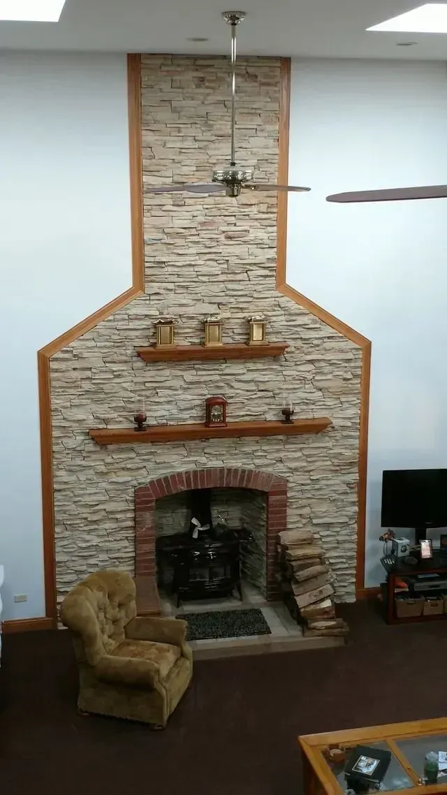 Fireplace with stacked stone facade, arched brick firebox, and wooden shelves. A chair sits in front.