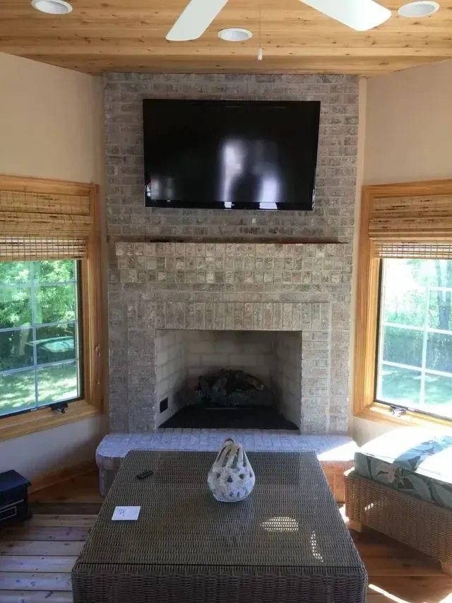 Fireplace with mounted TV, brick surround, wooden ceiling and trim, with windows on either side.