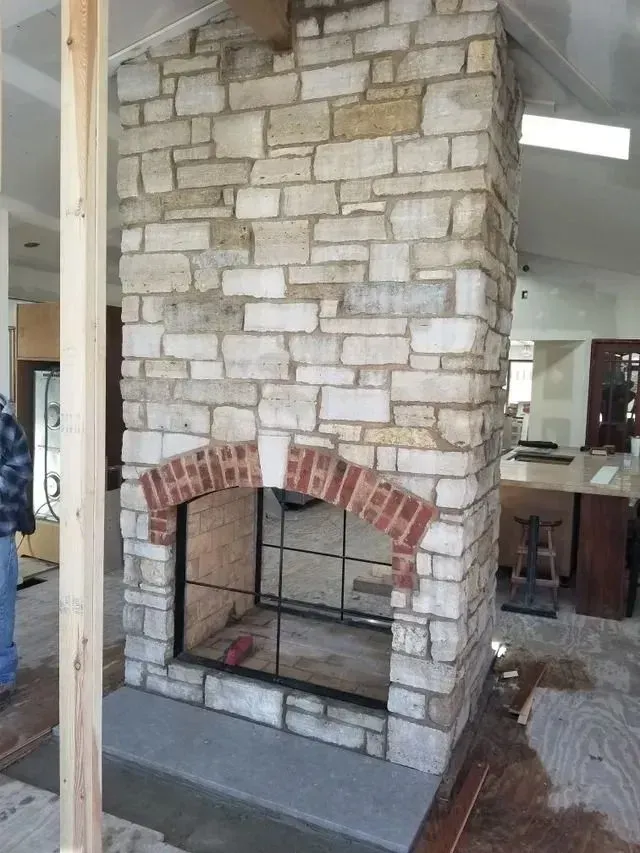 Stone fireplace with arched brick firebox in a home under construction.