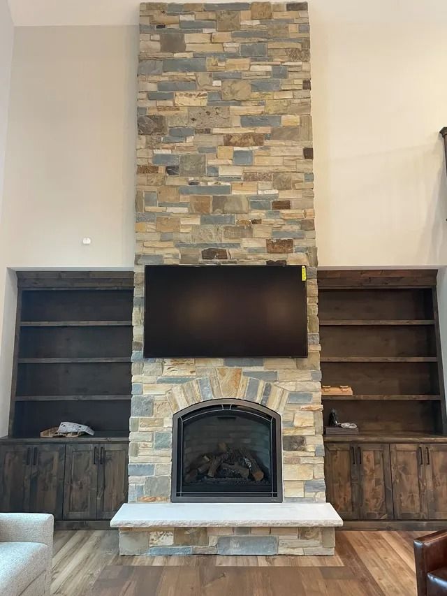 Fireplace with stone surround, a mounted TV, and built-in bookshelves.