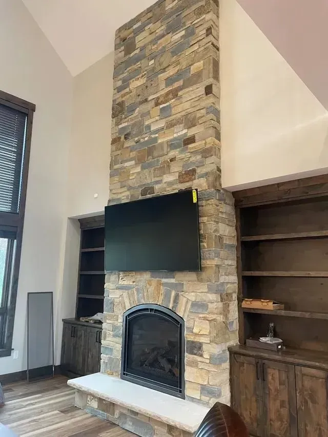 Stone fireplace with built-in bookshelves, mounted TV, and light wood floors.