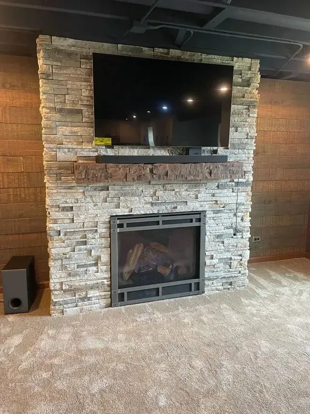 Fireplace with stone surround, TV above, and soundbar. Dark gray metal trim on the fireplace.