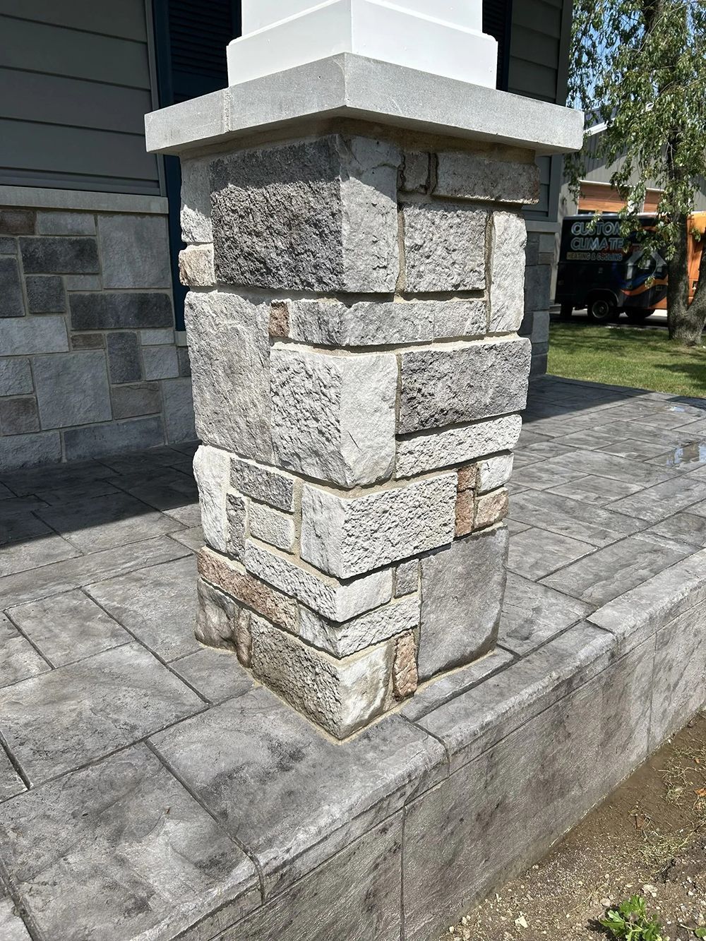 Stone pillar on a gray stone patio in front of a house.