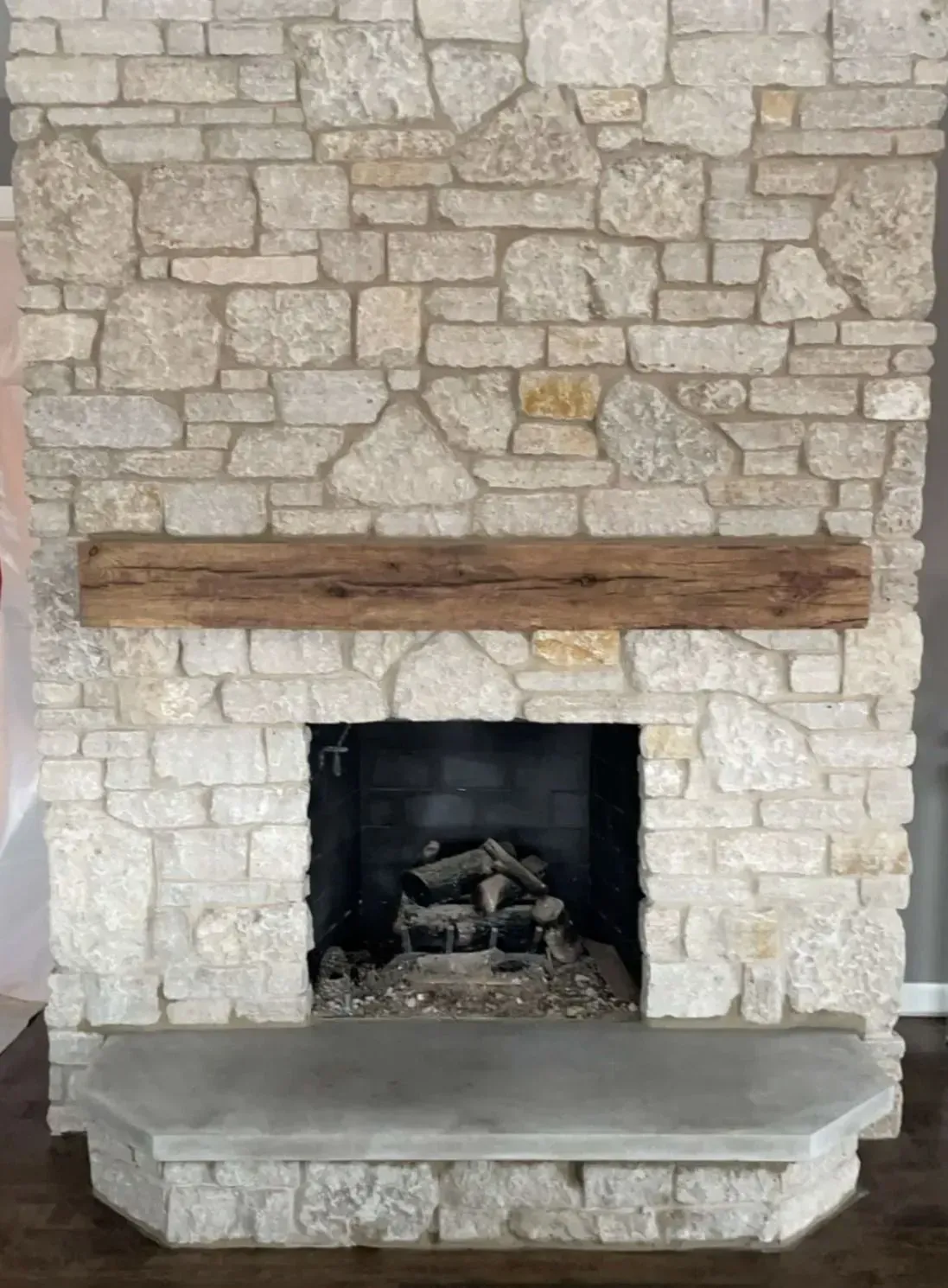 Stone fireplace with wooden mantle and concrete hearth. Fireplace opening with logs.