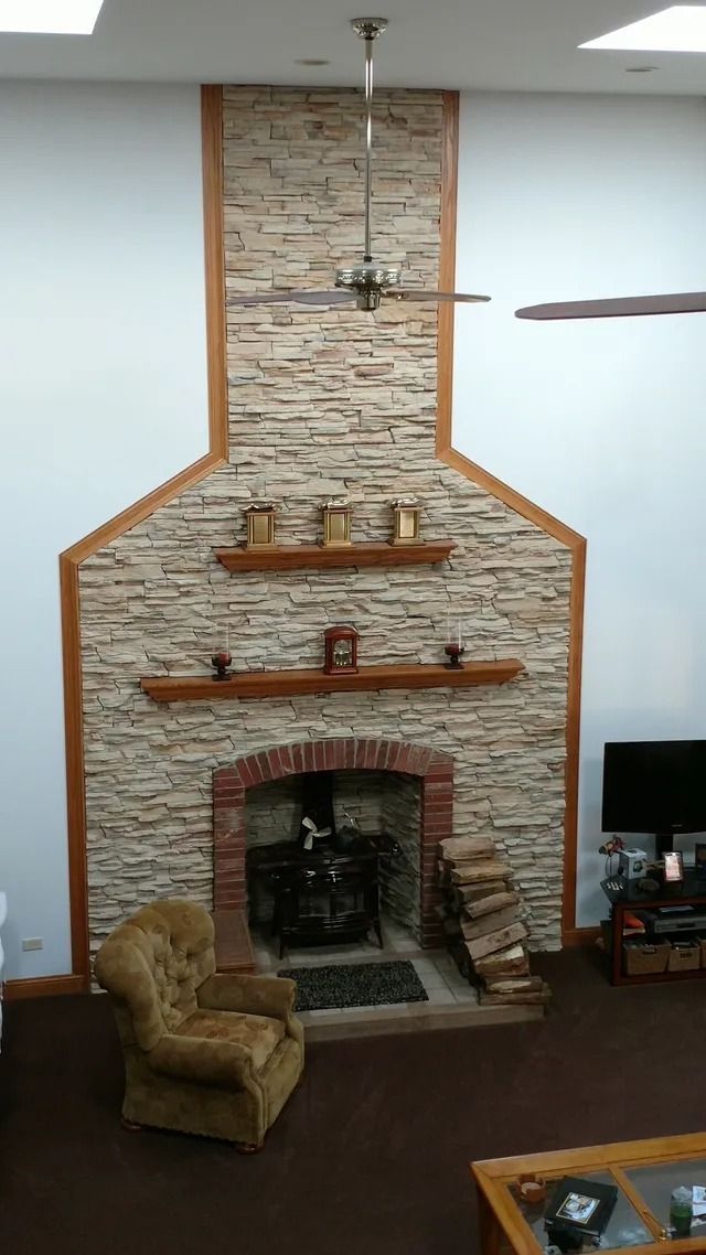 Fireplace with stacked stone facade, brick firebox, and wooden shelves. A brown armchair sits nearby.