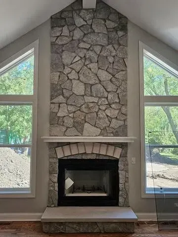 Stone fireplace with tall windows on either side, modern interior.