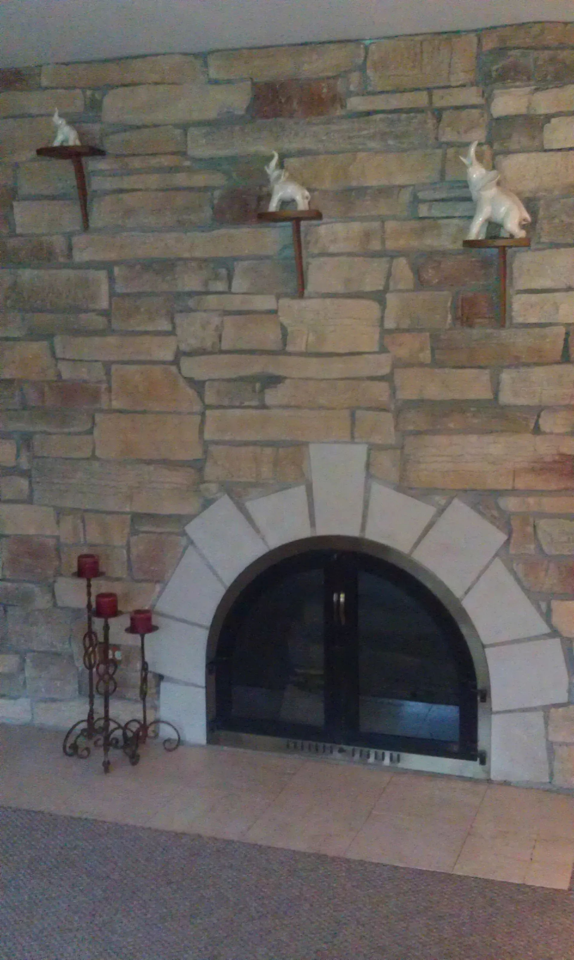 Stone fireplace with arched opening, white shelves with elephant figurines. Decorative metal candle holder.