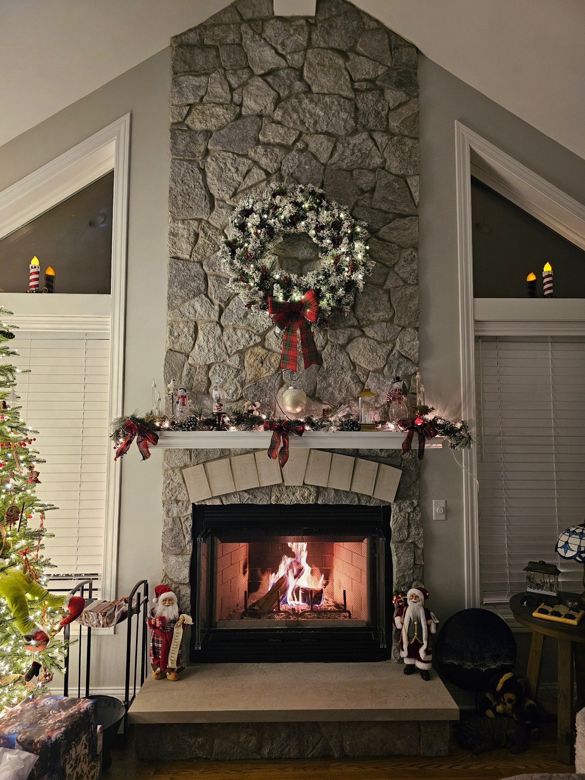 Fireplace with a lit fire, decorated for Christmas with a wreath and garland.