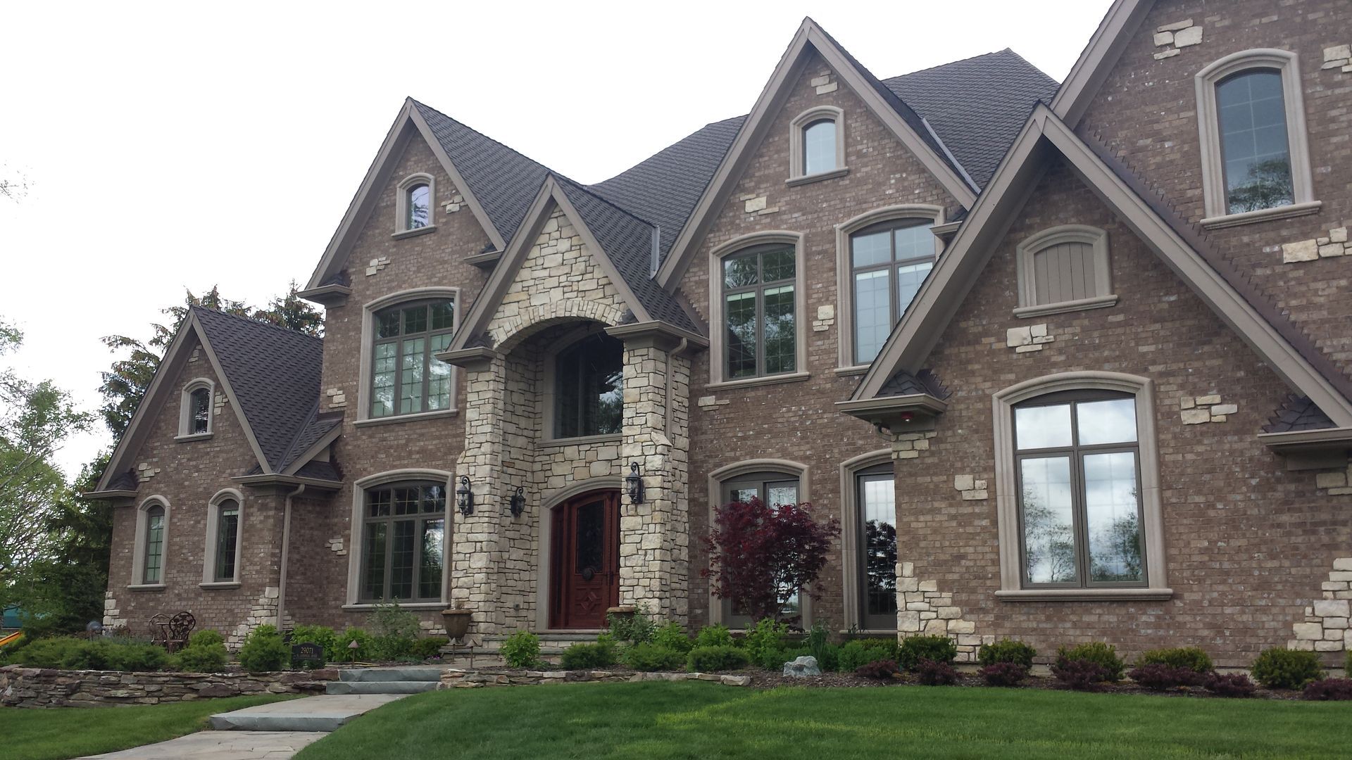 Brick house with stone accents, multiple gables, and a dark roof. Green lawn in front.