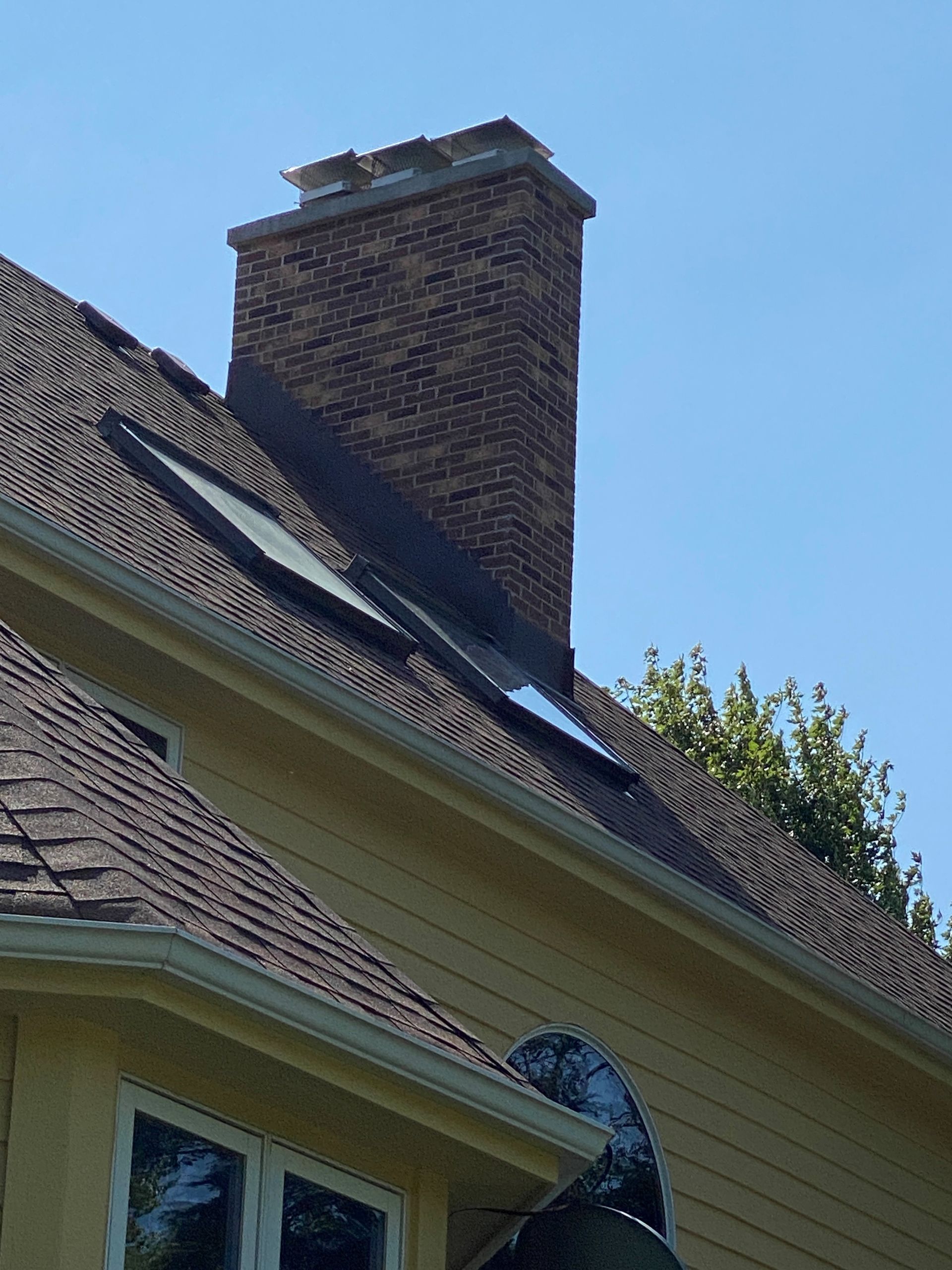 Brick chimney on a dark roof of a yellow house against a blue sky.