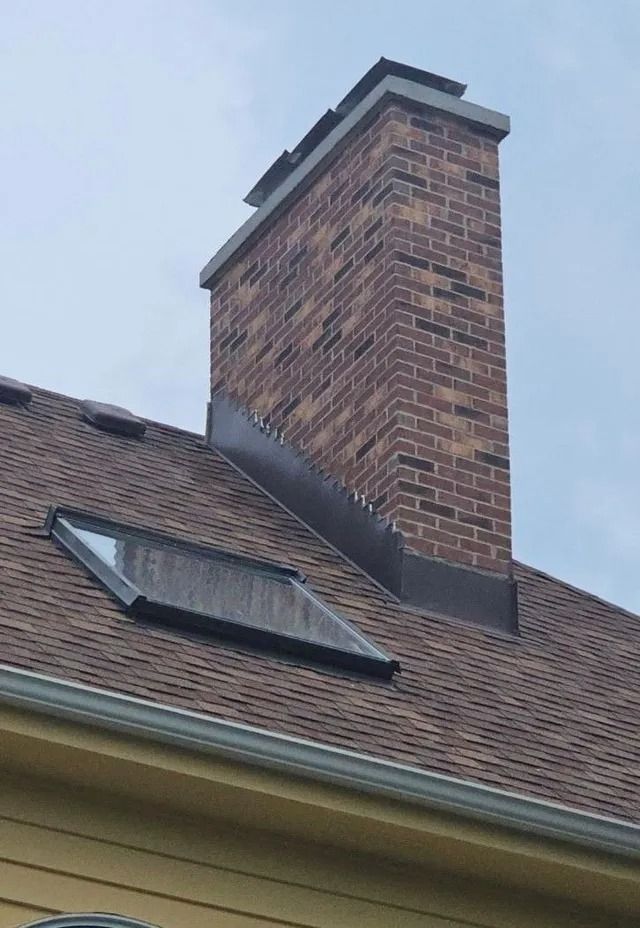 Brick chimney on a brown shingled roof with a dark-framed skylight.