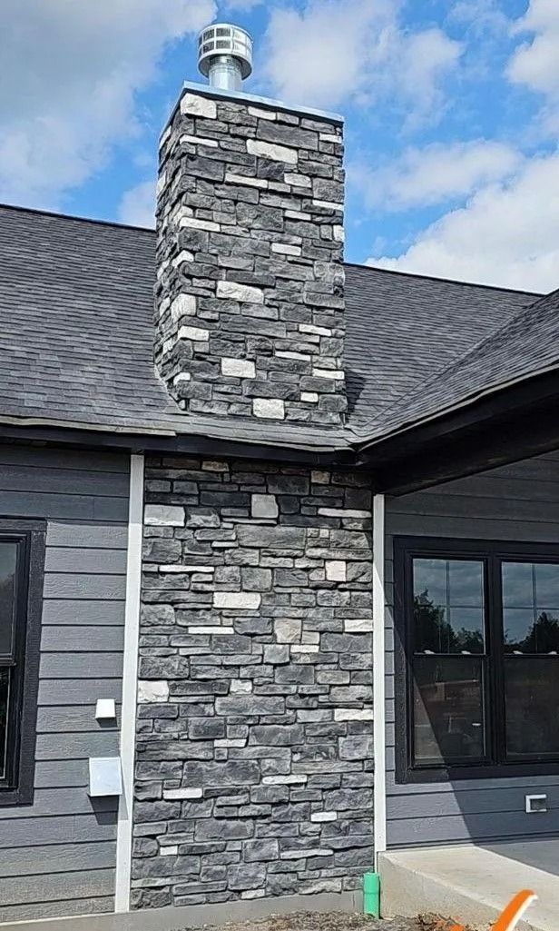 Stone chimney on a dark gray roof against a blue sky.