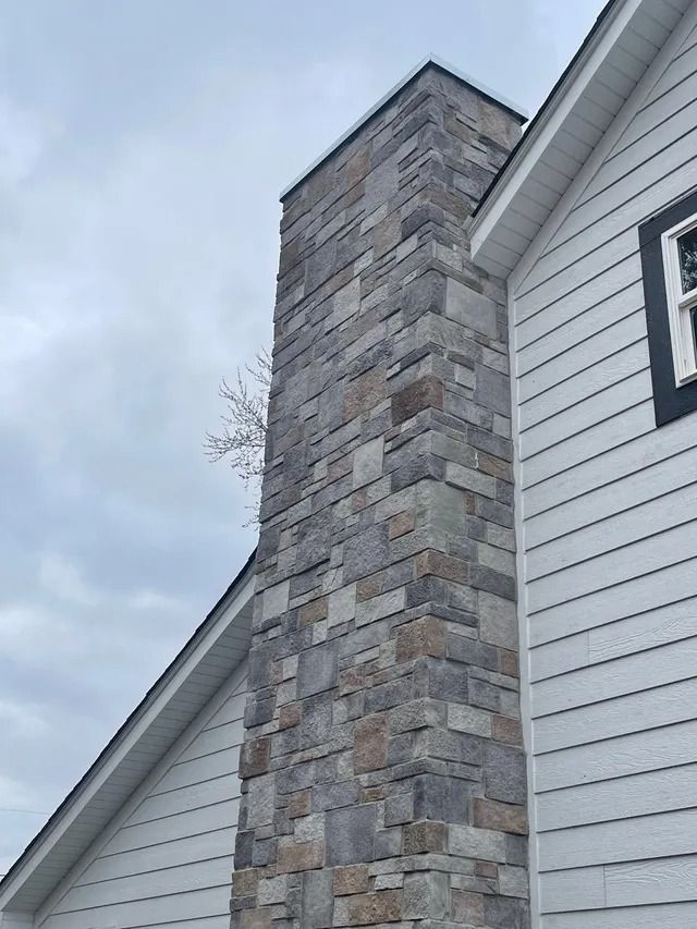 Stone chimney on a white-sided house against a cloudy sky.