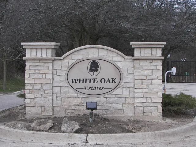 White Oak Estates entrance sign made of stone with an oak tree logo, oval shape, and pillars.
