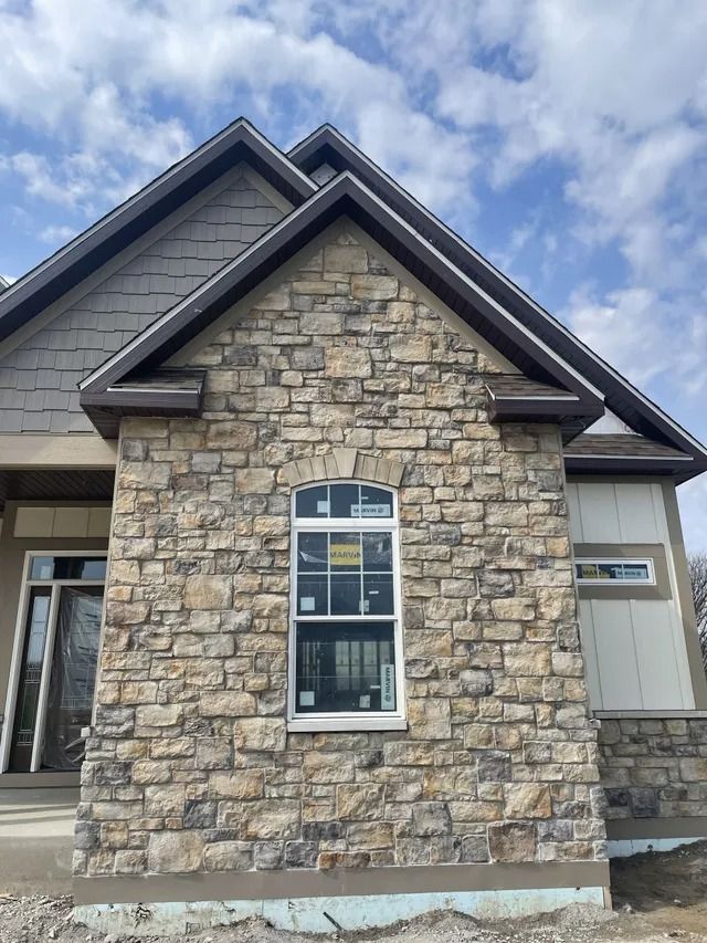 Stone facade with arched-top window under a brown-trimmed gable roof, against a cloudy sky.