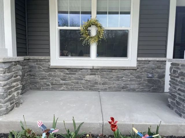 Two-story house with stone facade, arched window, and white garage door. Snow on lawn.
